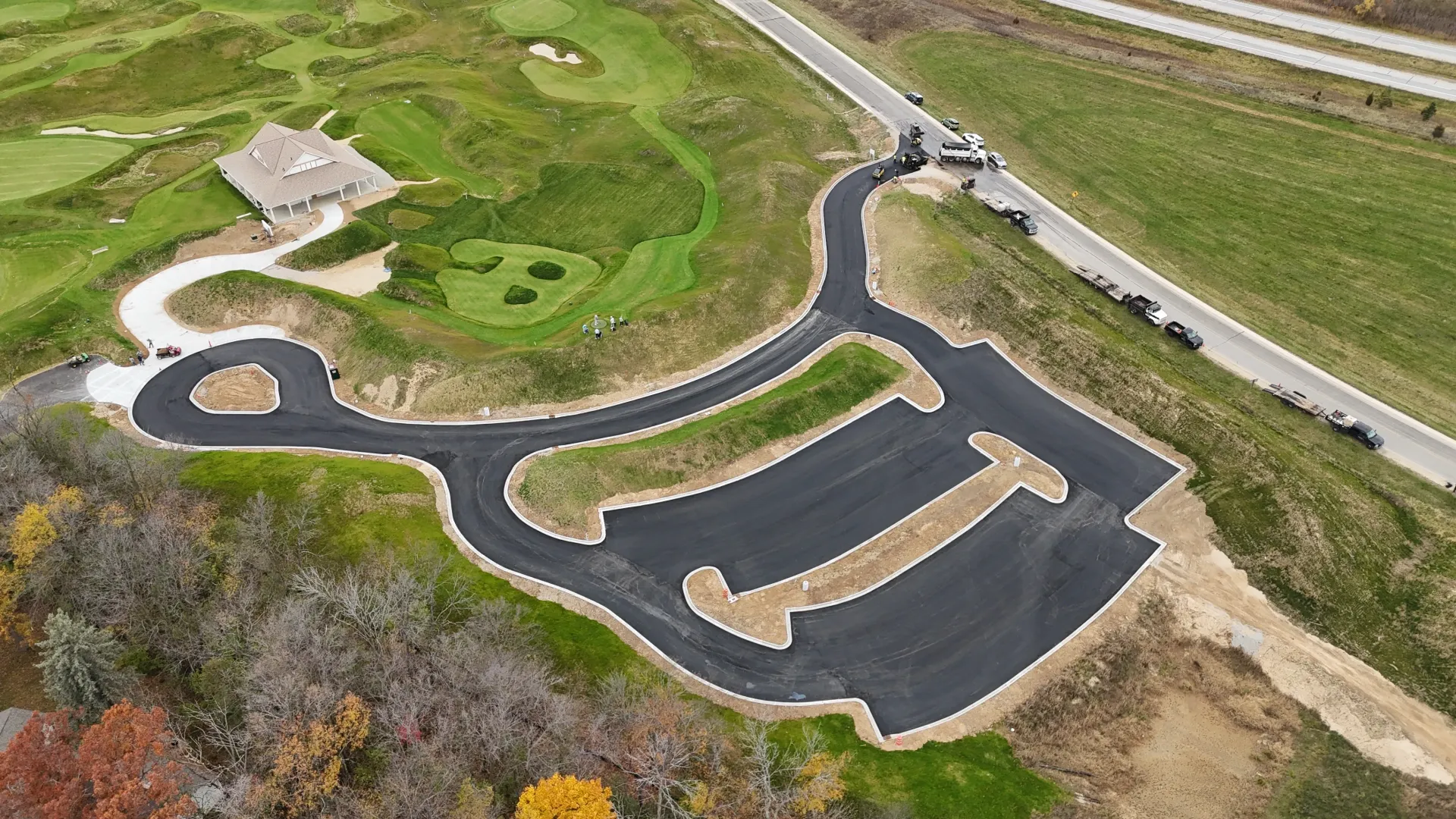 Aerial view of a paved pump track winding through a grassy park beside a road.