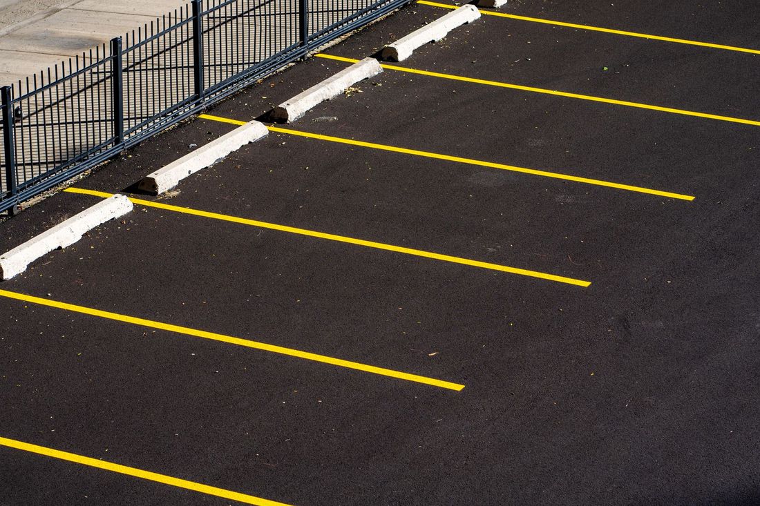 Empty parking lot with yellow lined spaces beside a black metal fence and sidewalk curb.