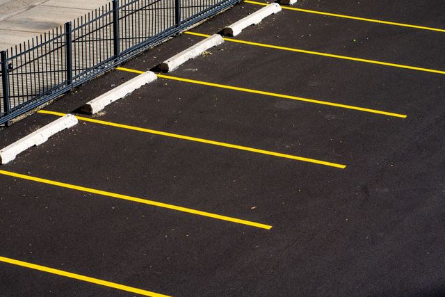 Empty parking lot with yellow lined spaces beside a black metal fence