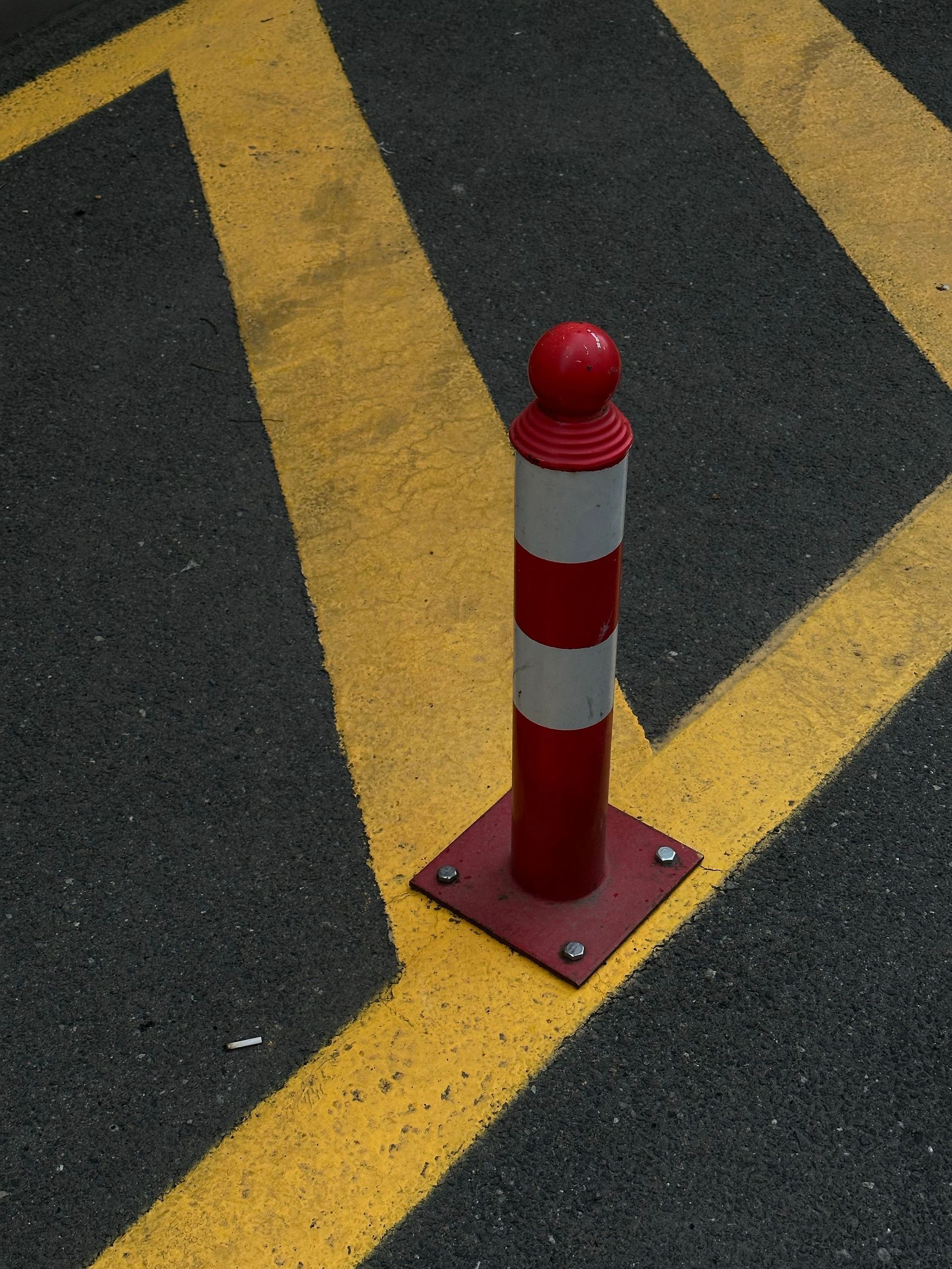 Red-and-white post on a yellow road marking over dark asphalt.