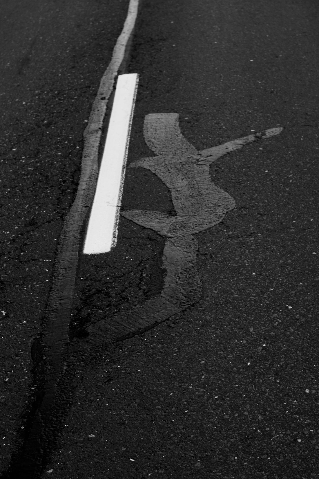 Damaged white lane marking on dark asphalt road with a faded patch and curb edge