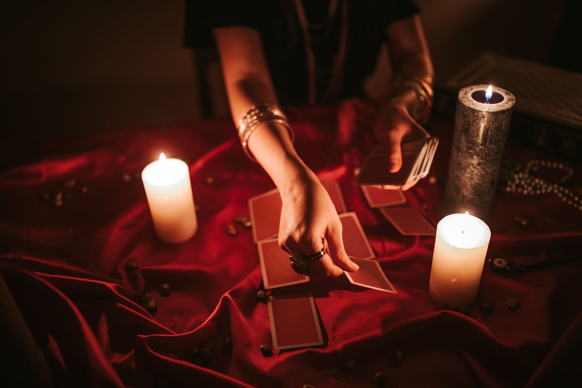 A female fortune teller reading tarot on a red velvet fabric with lighted candles.