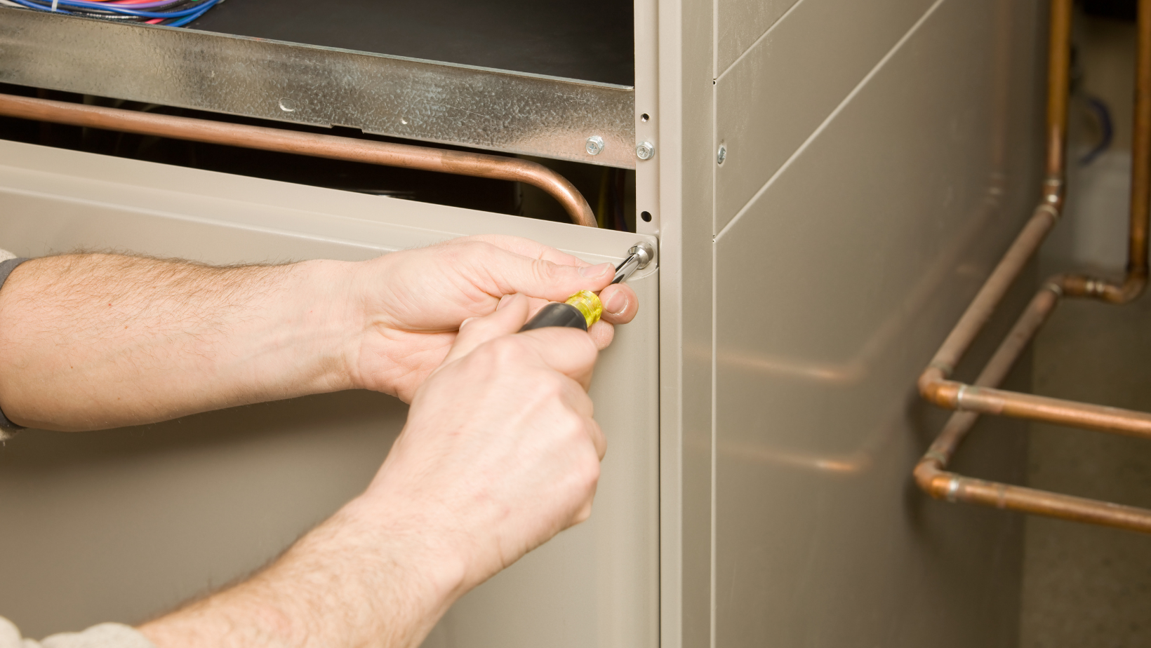 Person using a screwdriver to work on a beige heating system unit.