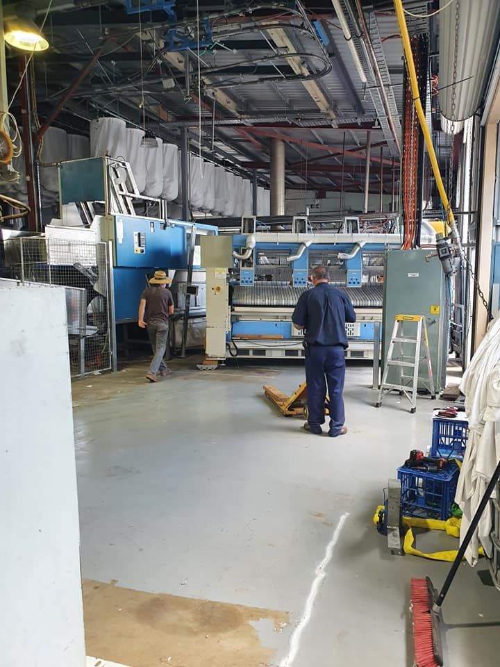 Two workers in a factory aisle near a large blue machine and overhead ducts