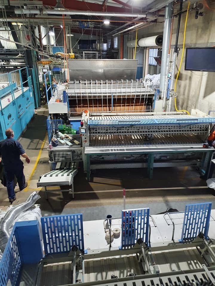 Industrial factory floor with large textile machinery and a worker standing beside it