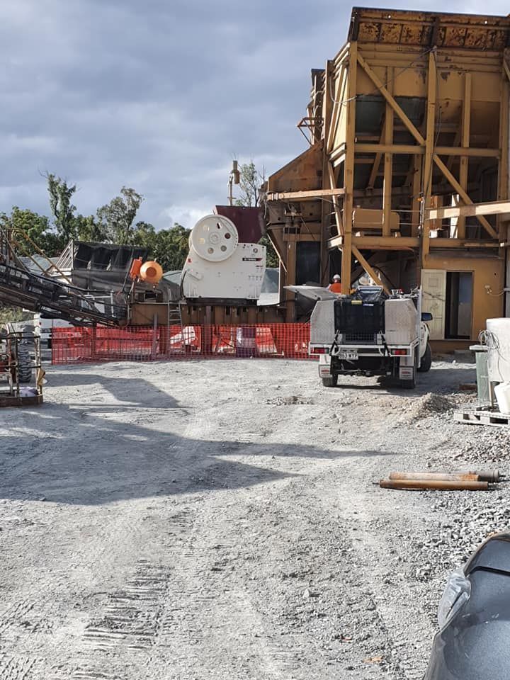 Construction site with heavy machinery, a large industrial structure, and trucks on a gravel lot
