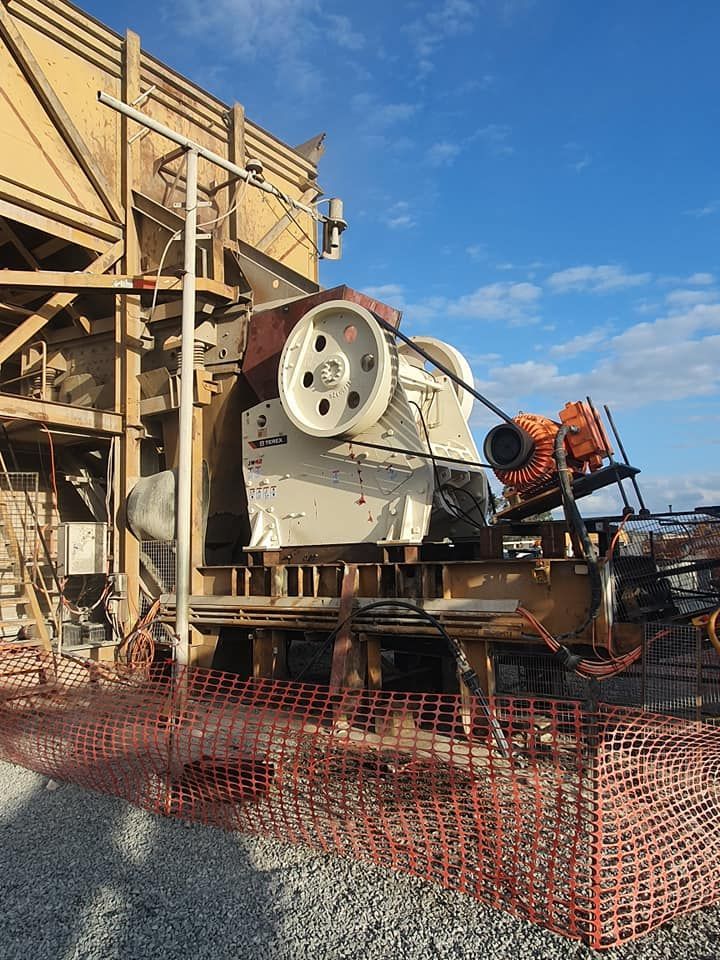 Industrial machinery at a construction site with wooden scaffolding and orange safety fencing under a blue sky