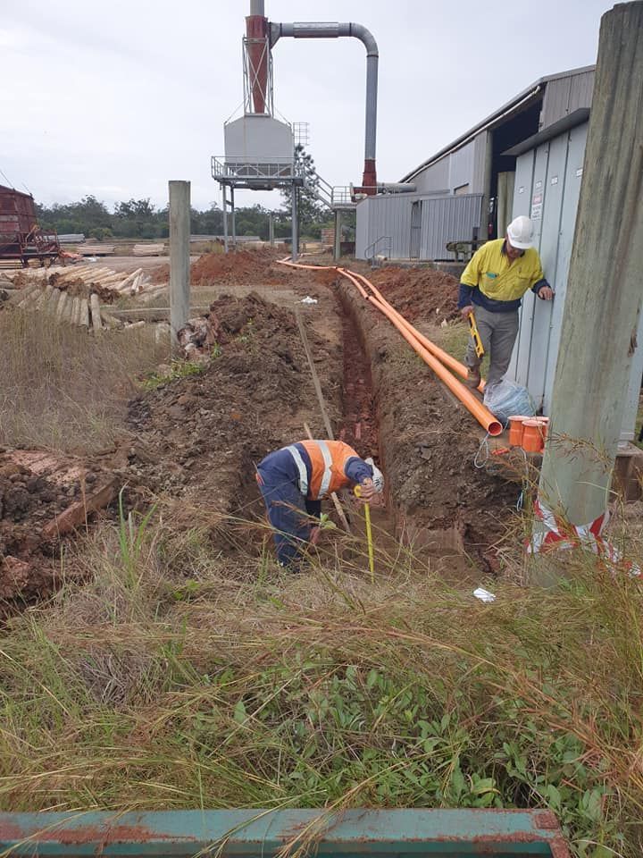 Construction workers installing utility lines in a trench beside a building and excavator