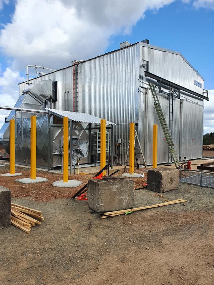 Industrial metal building with yellow support posts, stairs, and equipment under a cloudy sky