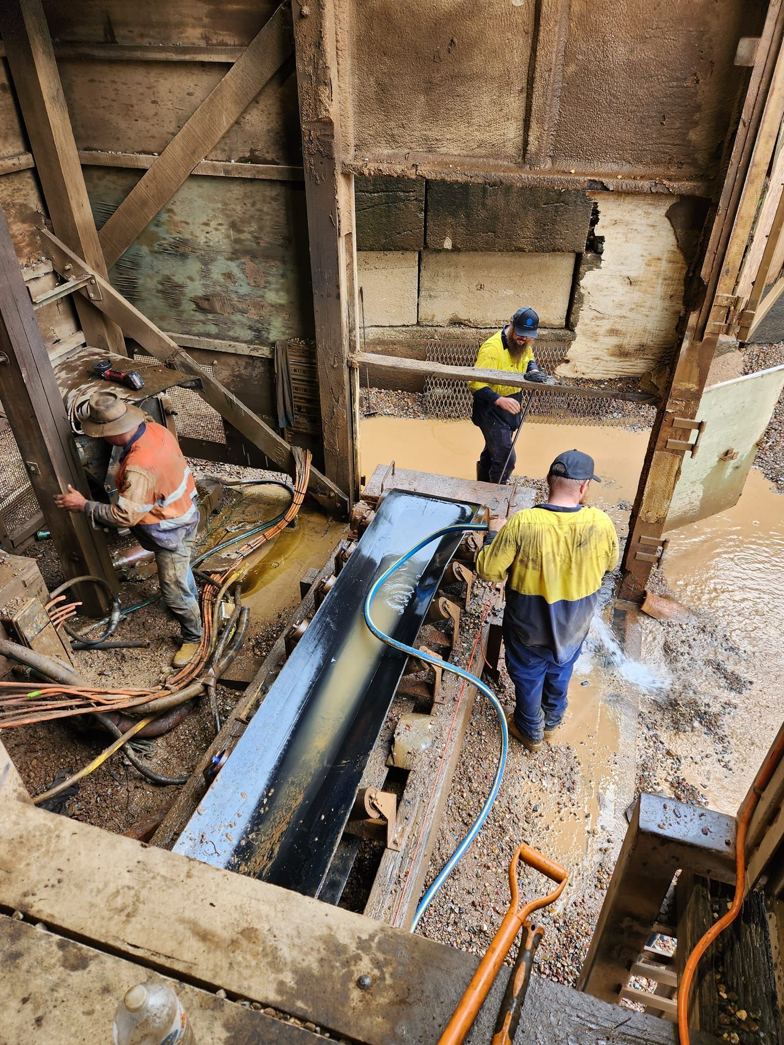 Workers in a concrete pit guiding a large blue pipe during construction work