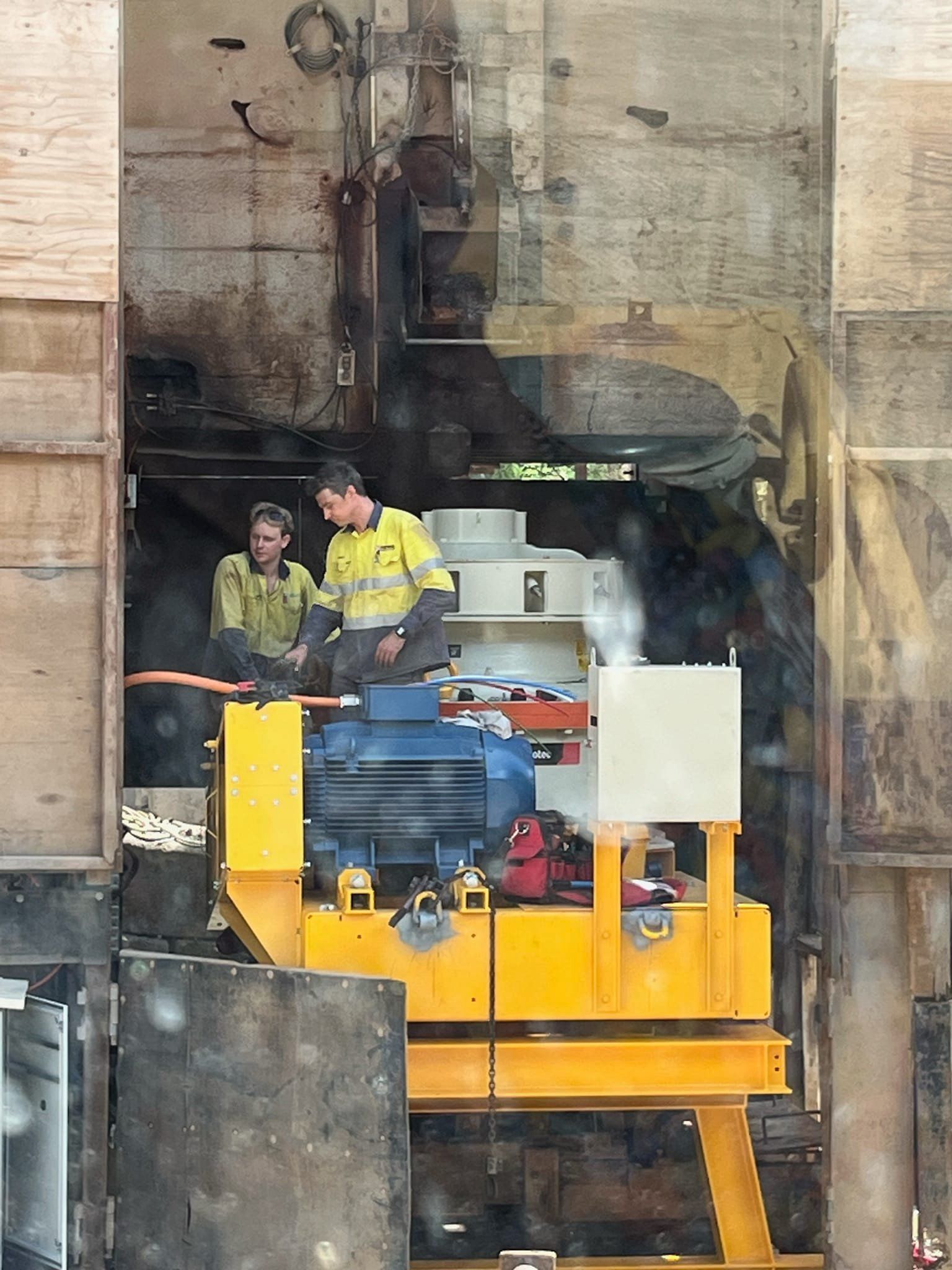 Two workers standing beside a large yellow industrial machine in a workshop