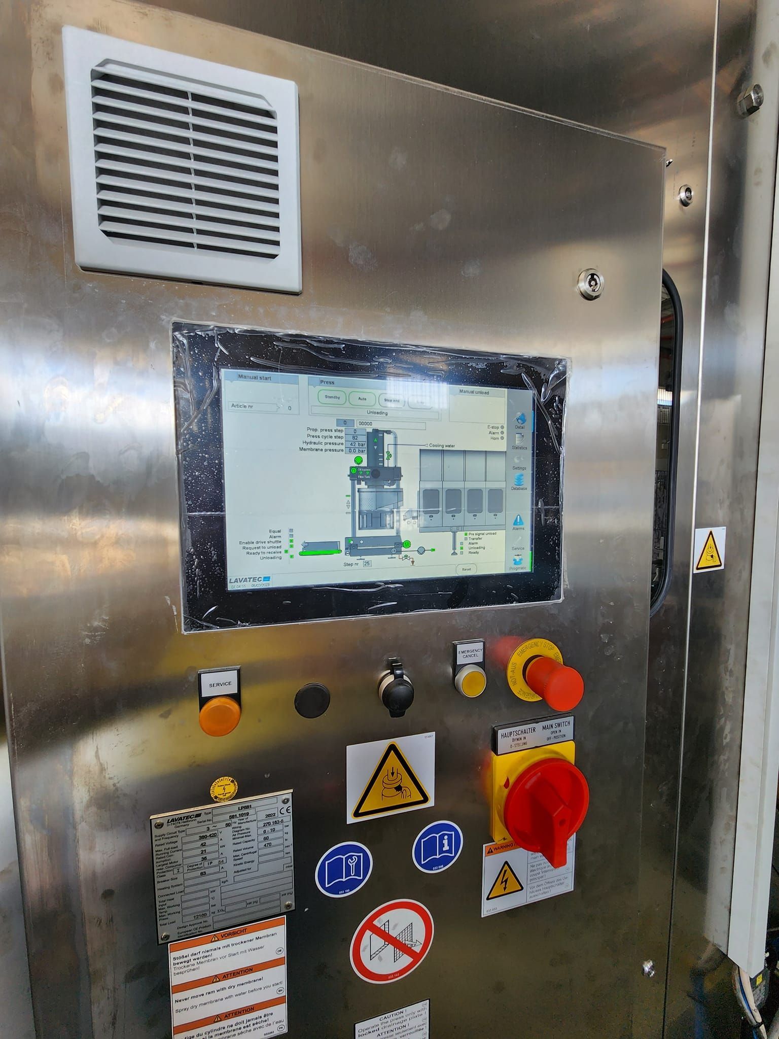 Industrial control panel with touchscreen, buttons, warning labels, and emergency stop in a metal enclosure