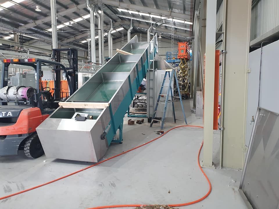 Industrial conveyor belt in a warehouse, with a forklift and orange cable on the floor.