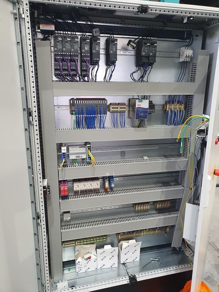 Open electrical control cabinet with rows of wires, circuit modules, and relays inside.