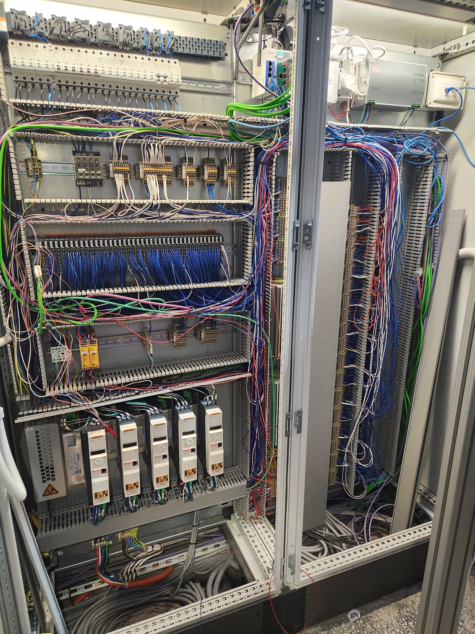 Open electrical control cabinets with dense wiring, relays, and circuit modules in an industrial panel.