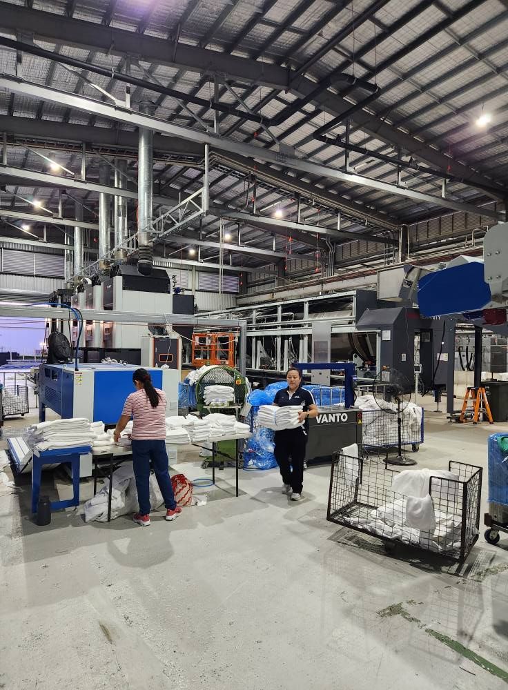 Industrial factory floor with workers, machinery, and metal racks under a high steel roof