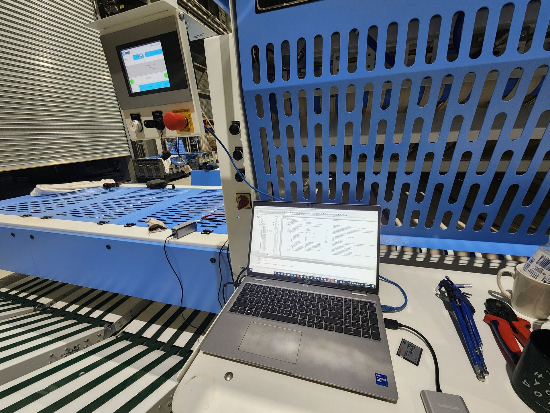 Laptop on industrial workstation beside blue machine panel and control screen in a factory setting