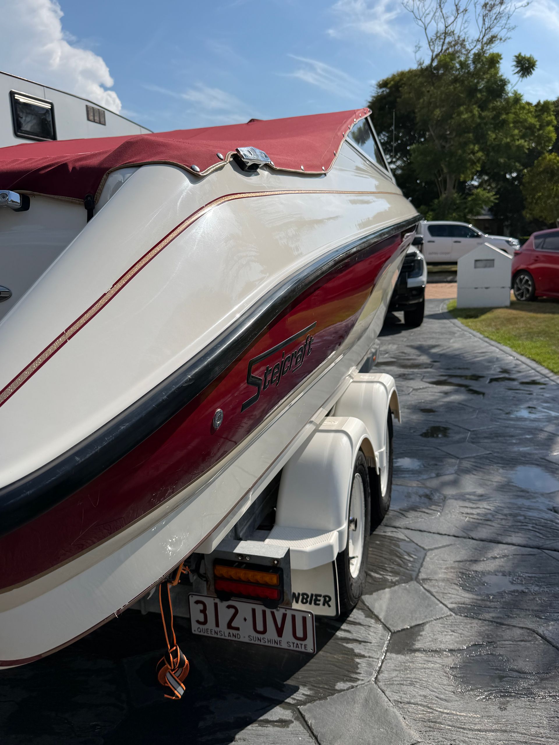 A cream and red motorboat on a trailer parked on a driveway with a car in the background.