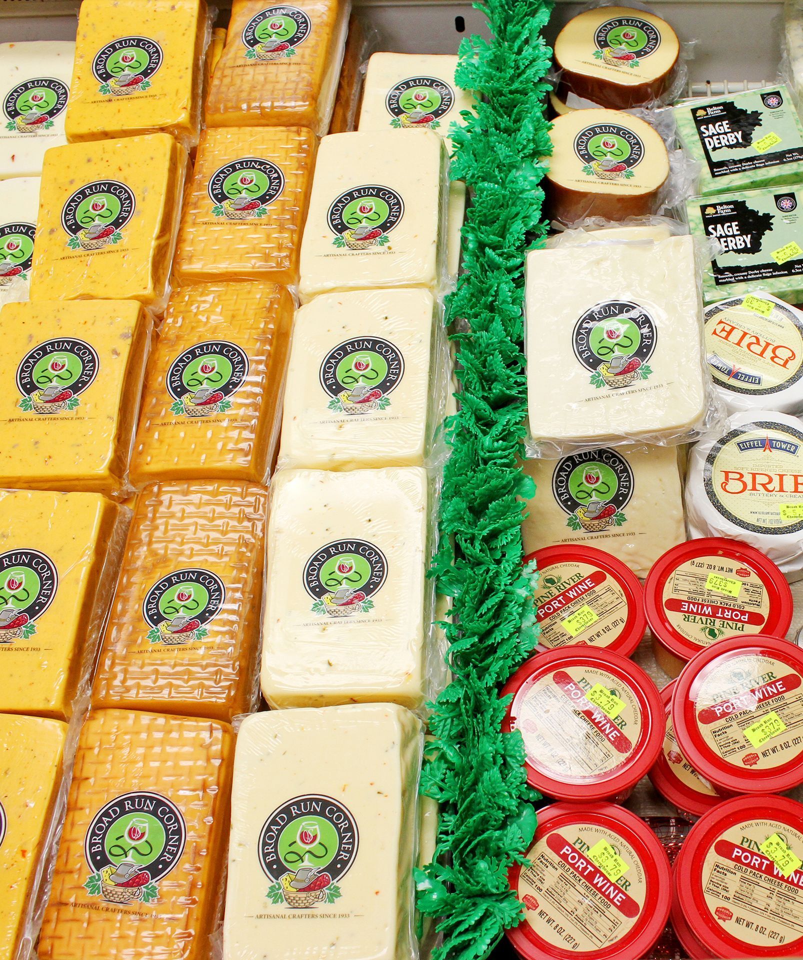 Display case filled with various cheeses; yellow, white, and red in color.