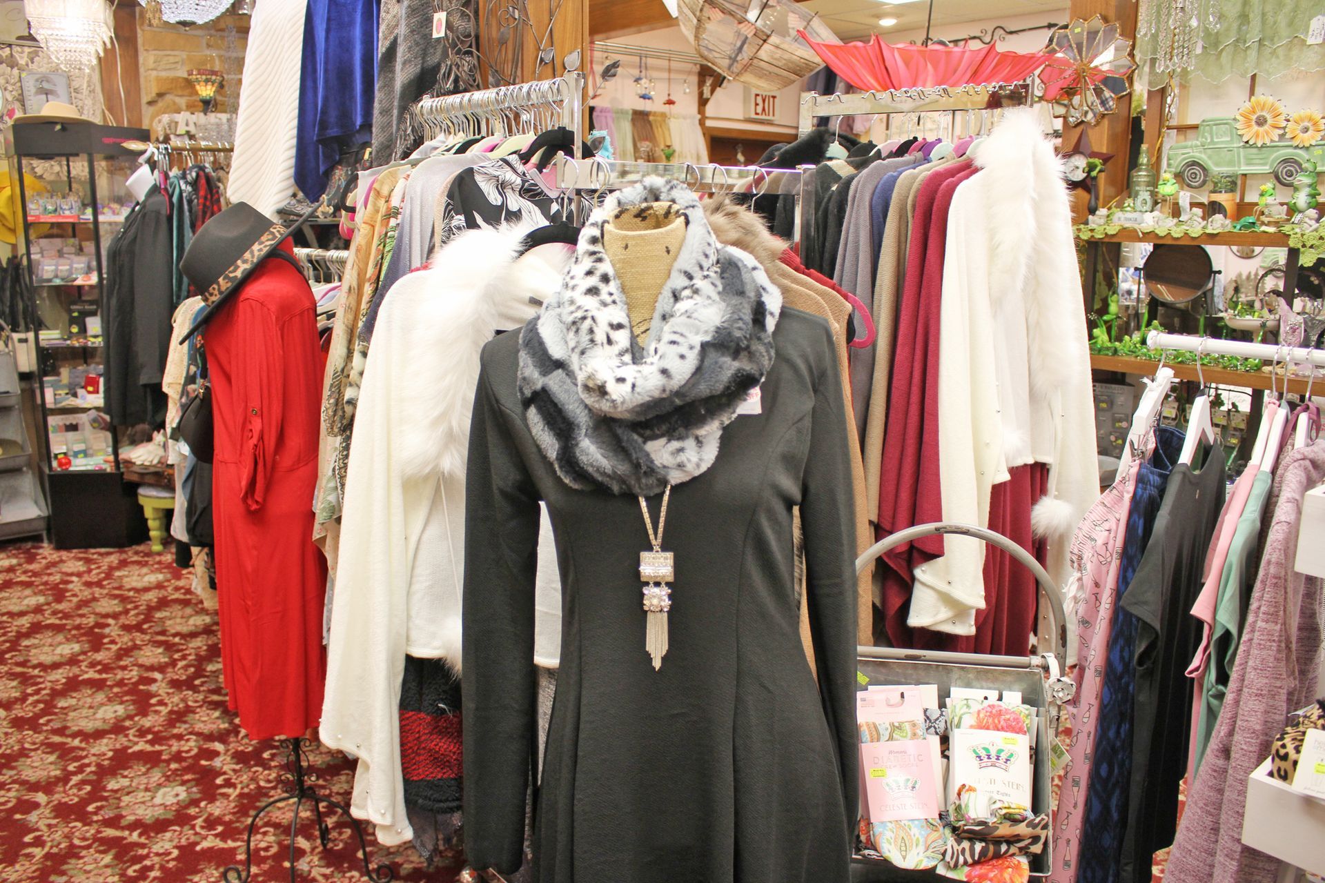 Mannequin in a retail store wearing a black dress and scarf. Clothing racks filled with various garments.