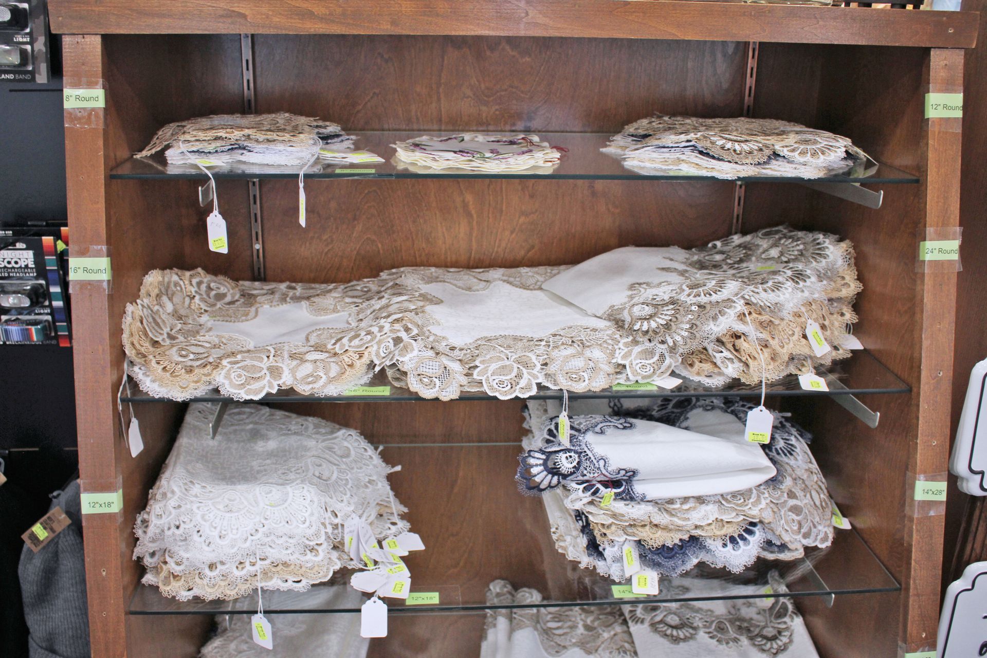 Wooden shelf displaying antique lace tablecloths and doilies with price tags.