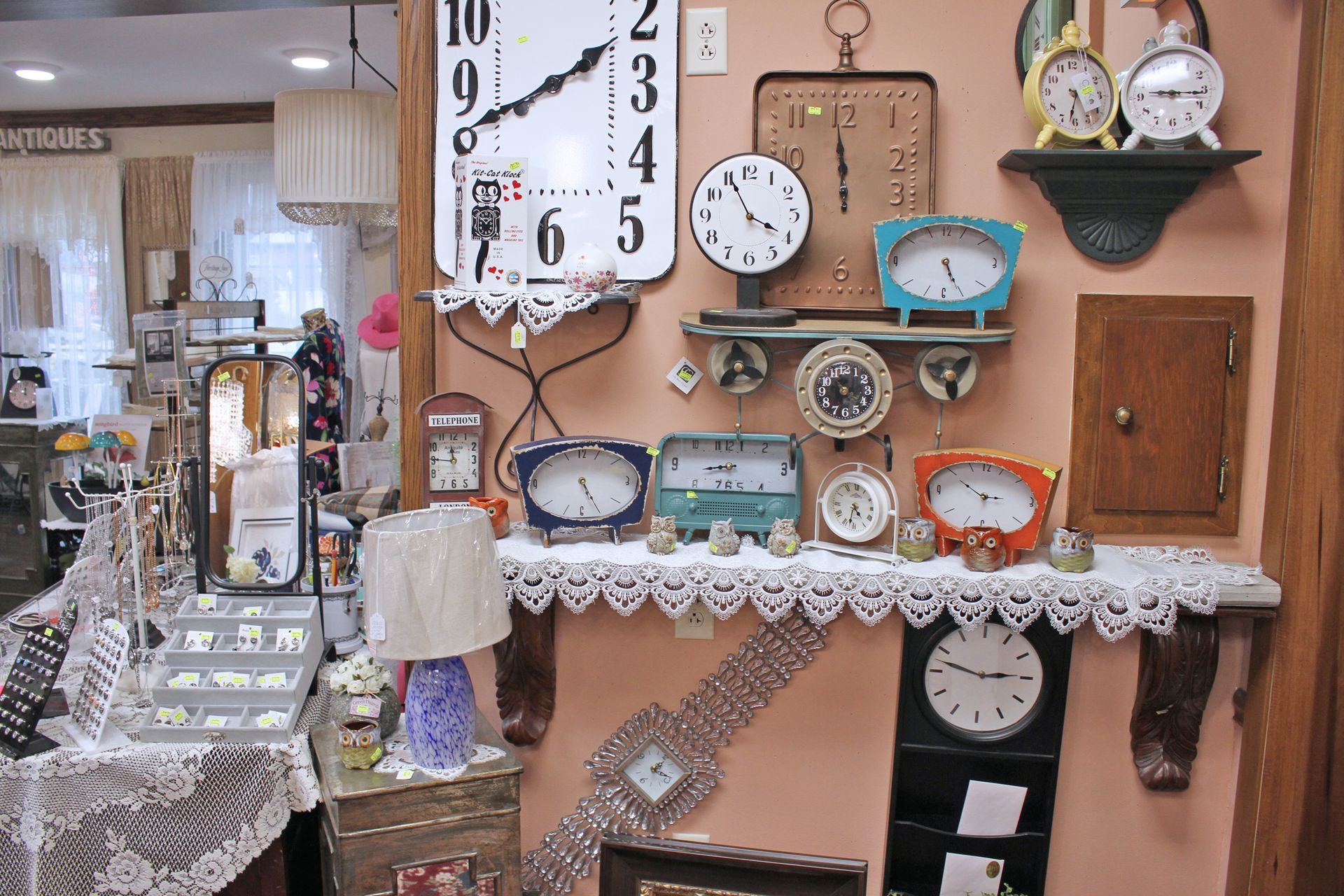 A display of vintage clocks and other decor inside a shop, with a pink wall as background.