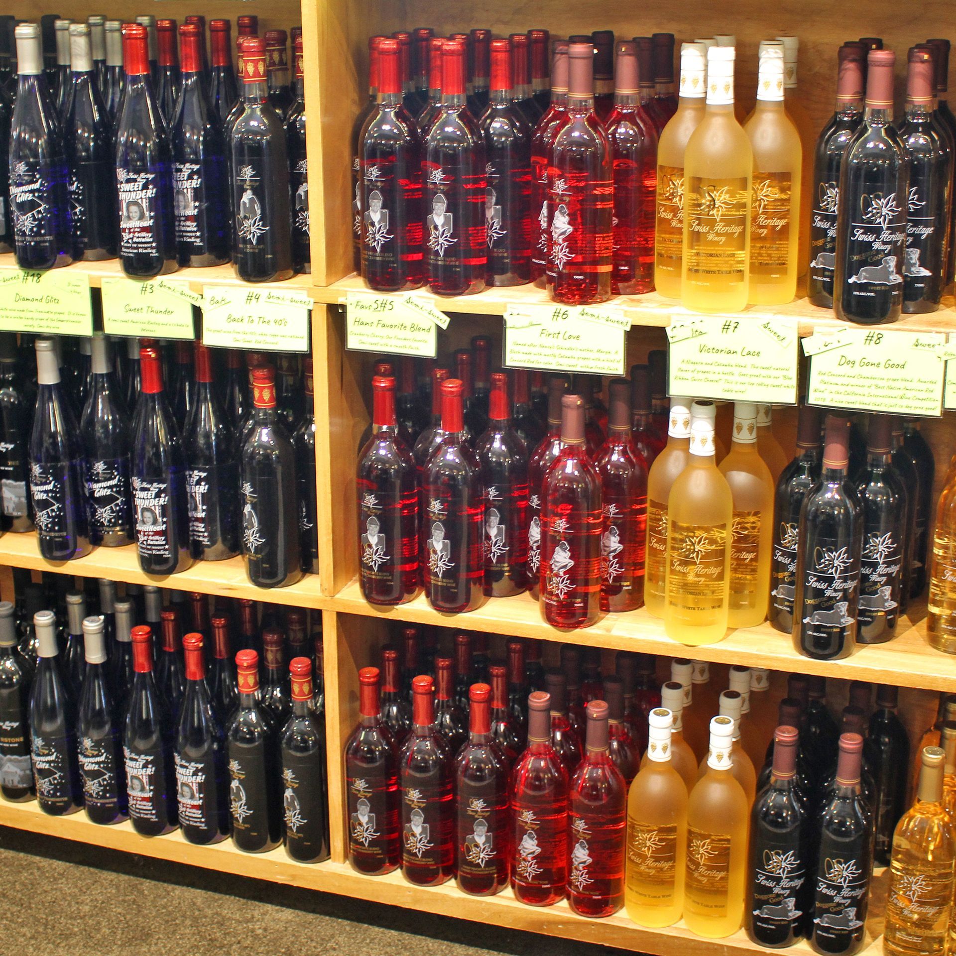 Shelves stocked with various wine bottles in a shop. Red, white, and dark bottles displayed with price tags.
