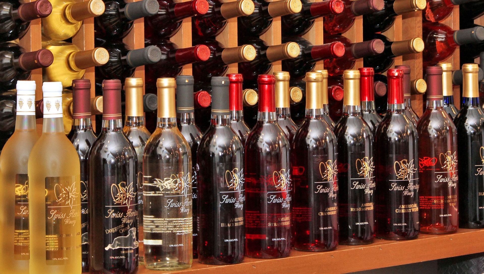 Wine bottles on display in a store, varied colors, labels visible, wooden shelves in the background.
