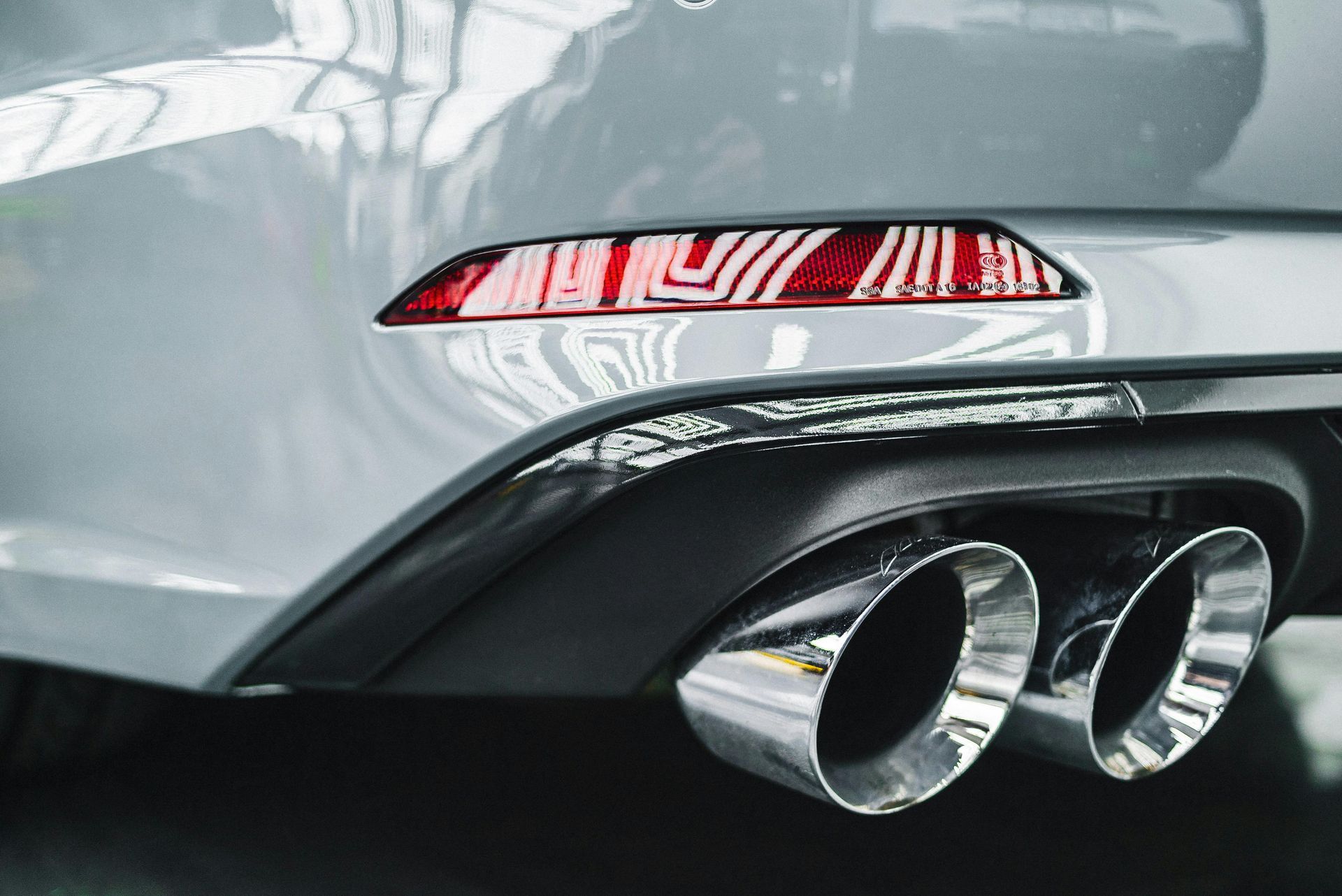A red car with a stainless steel exhaust pipe is parked on the side of the road.