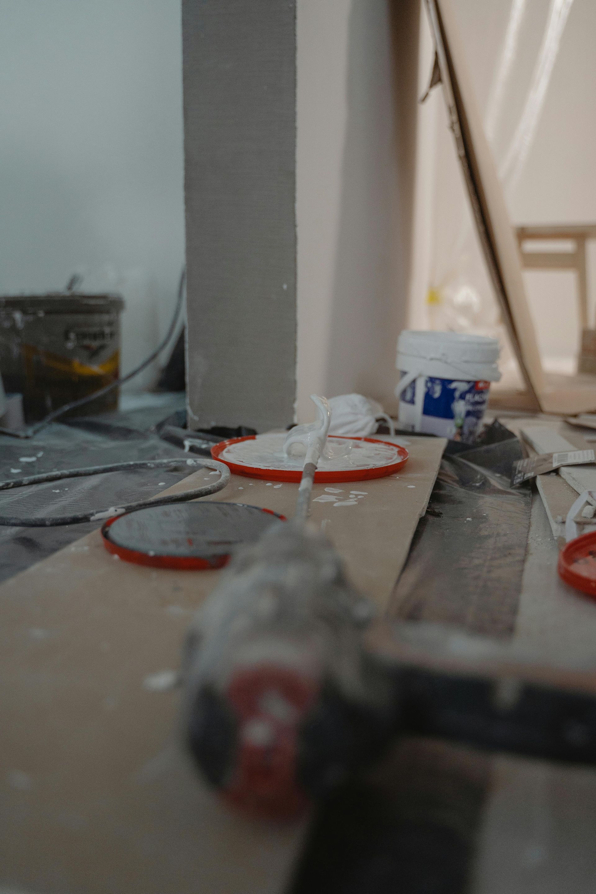Construction site: paint rollers, lids, and materials on the floor; white and neutral colors.