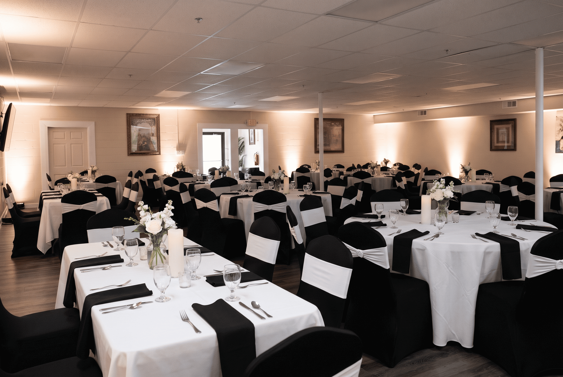 Banquet hall set for an event, with round tables covered in white linens and black chair covers.