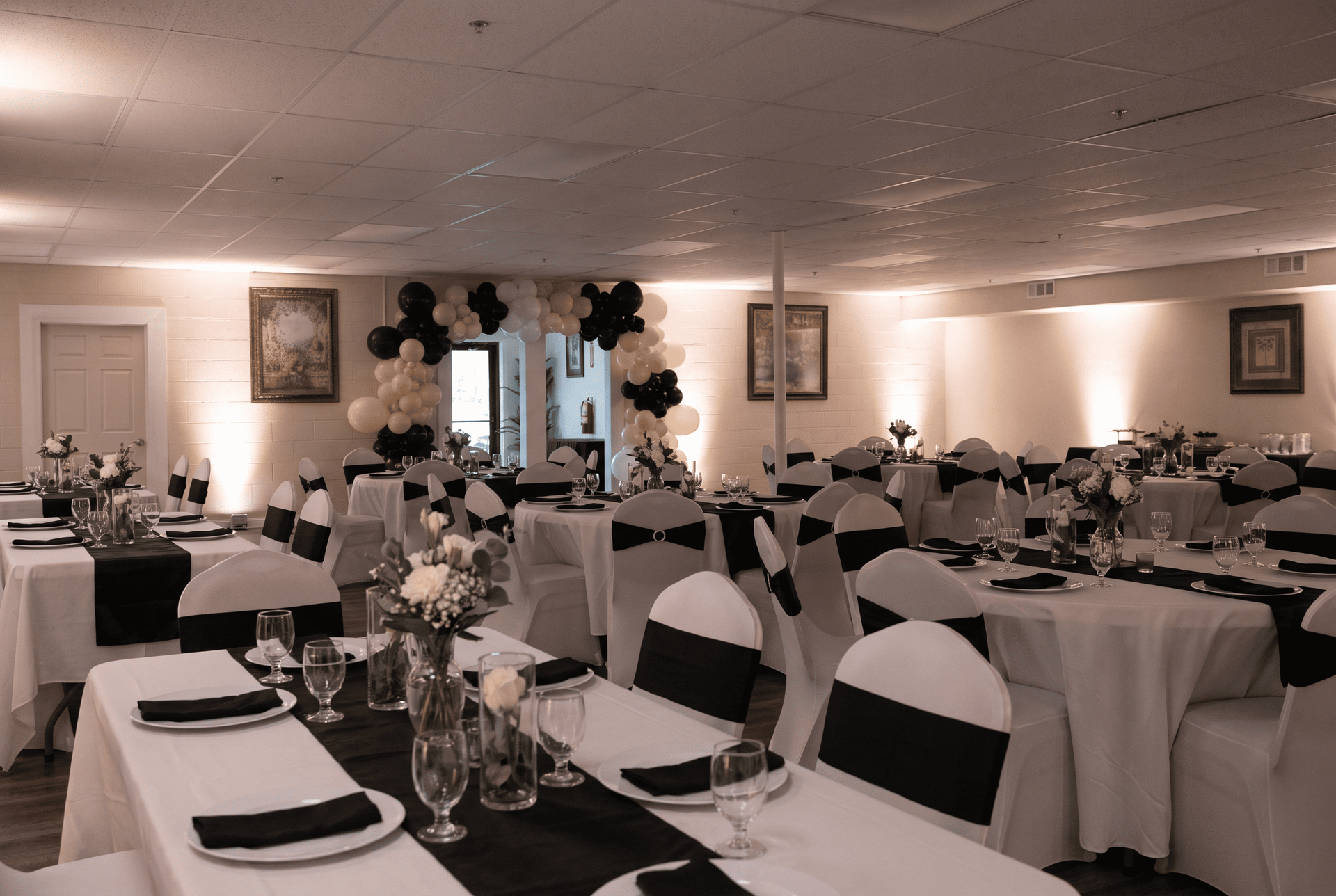 Decorated banquet hall with round tables, black and white chairs, and floral centerpieces