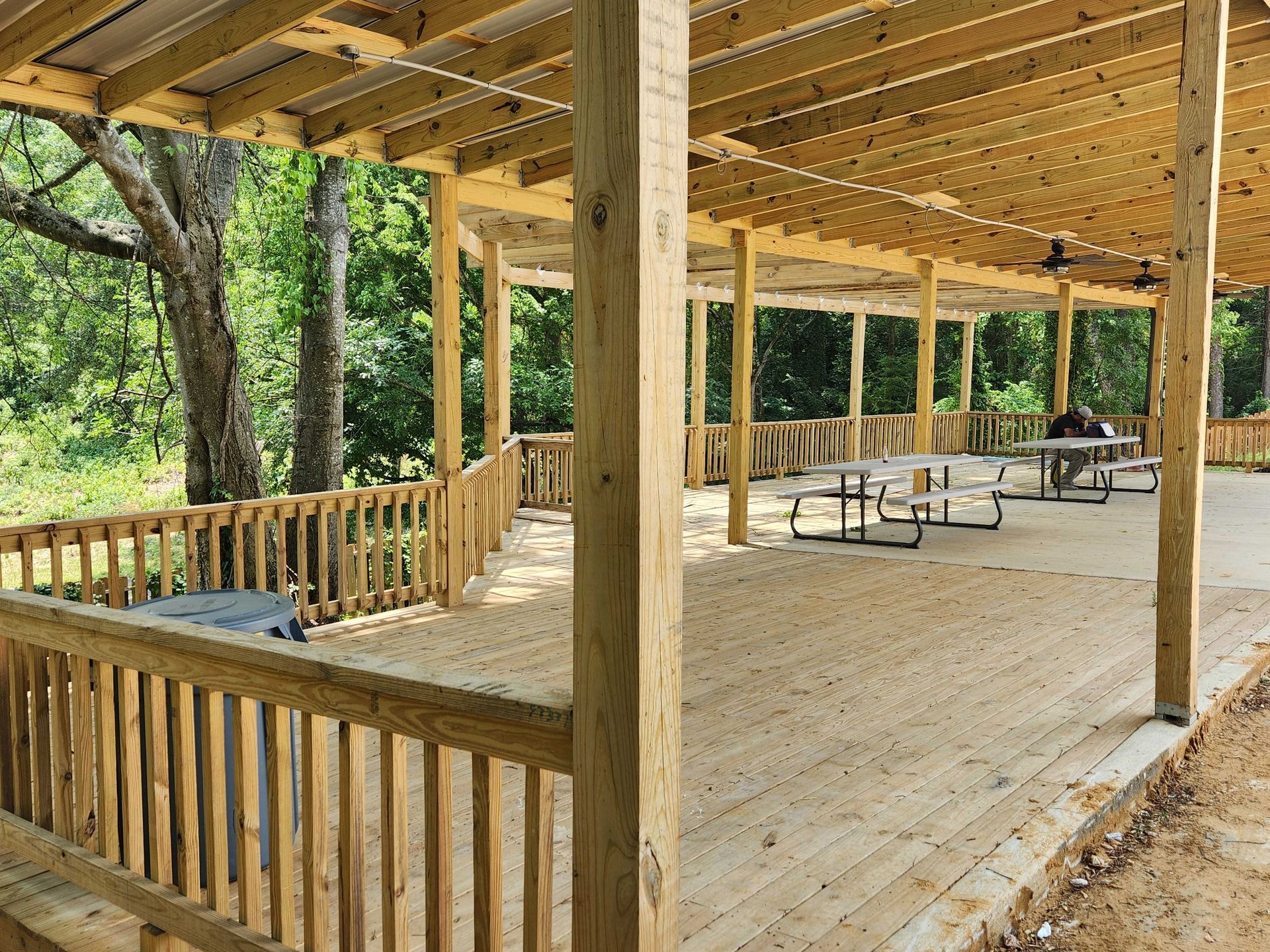 A wooden deck with tables and benches under a covered area.