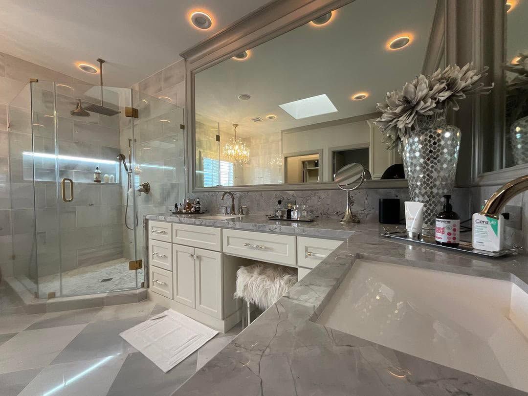 Luxury bathroom with glass shower, marble vanity, and large mirror-lit sink area