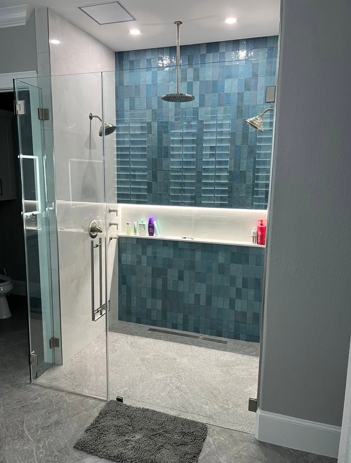 Modern bathroom with glass shower, blue tile accent wall, and a floating vanity with mirror