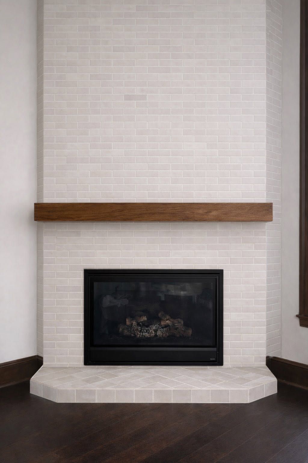White brick fireplace with wooden mantel and black hearth in a room with dark wood floors