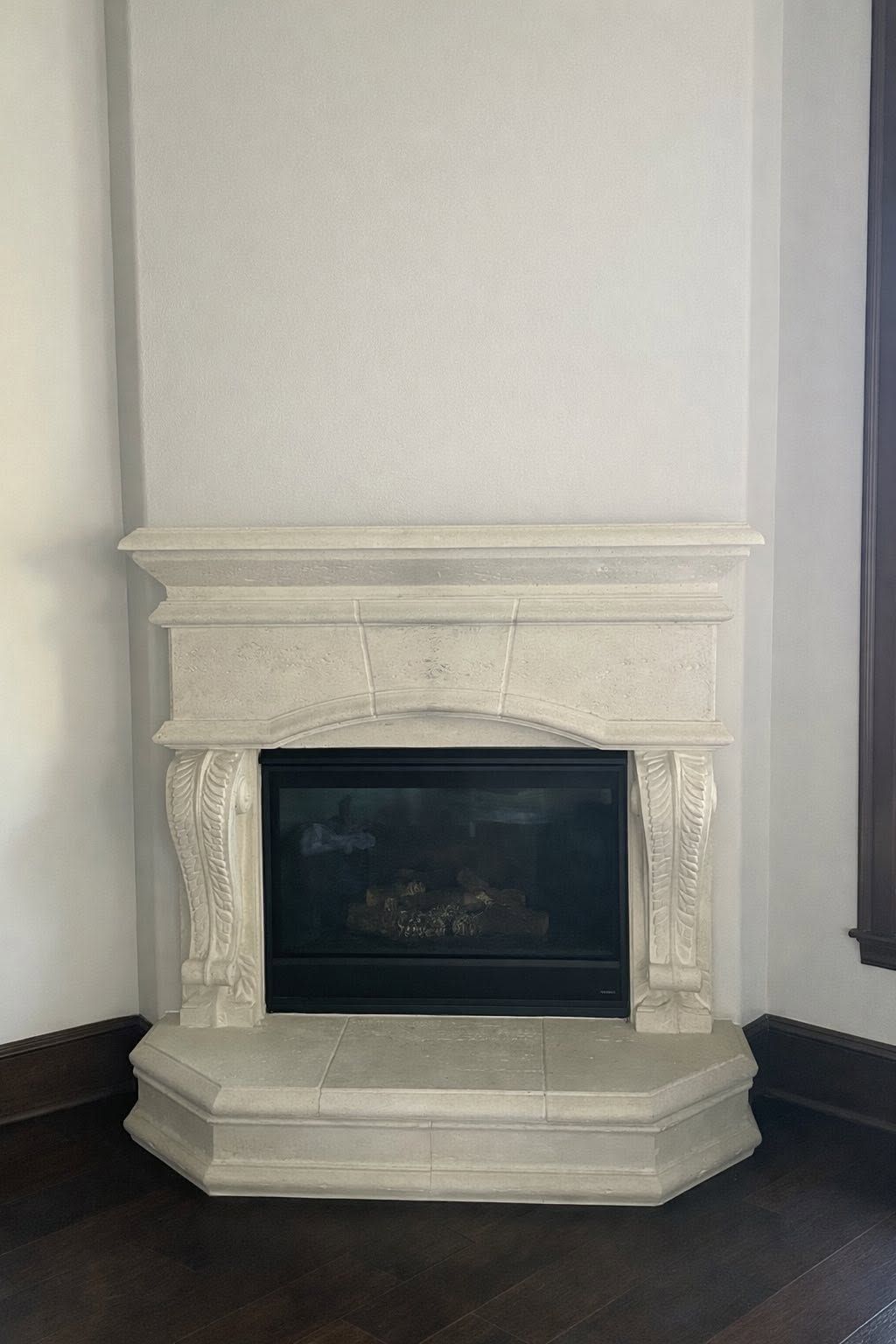 White ornate fireplace with carved details in a room corner against pale walls.