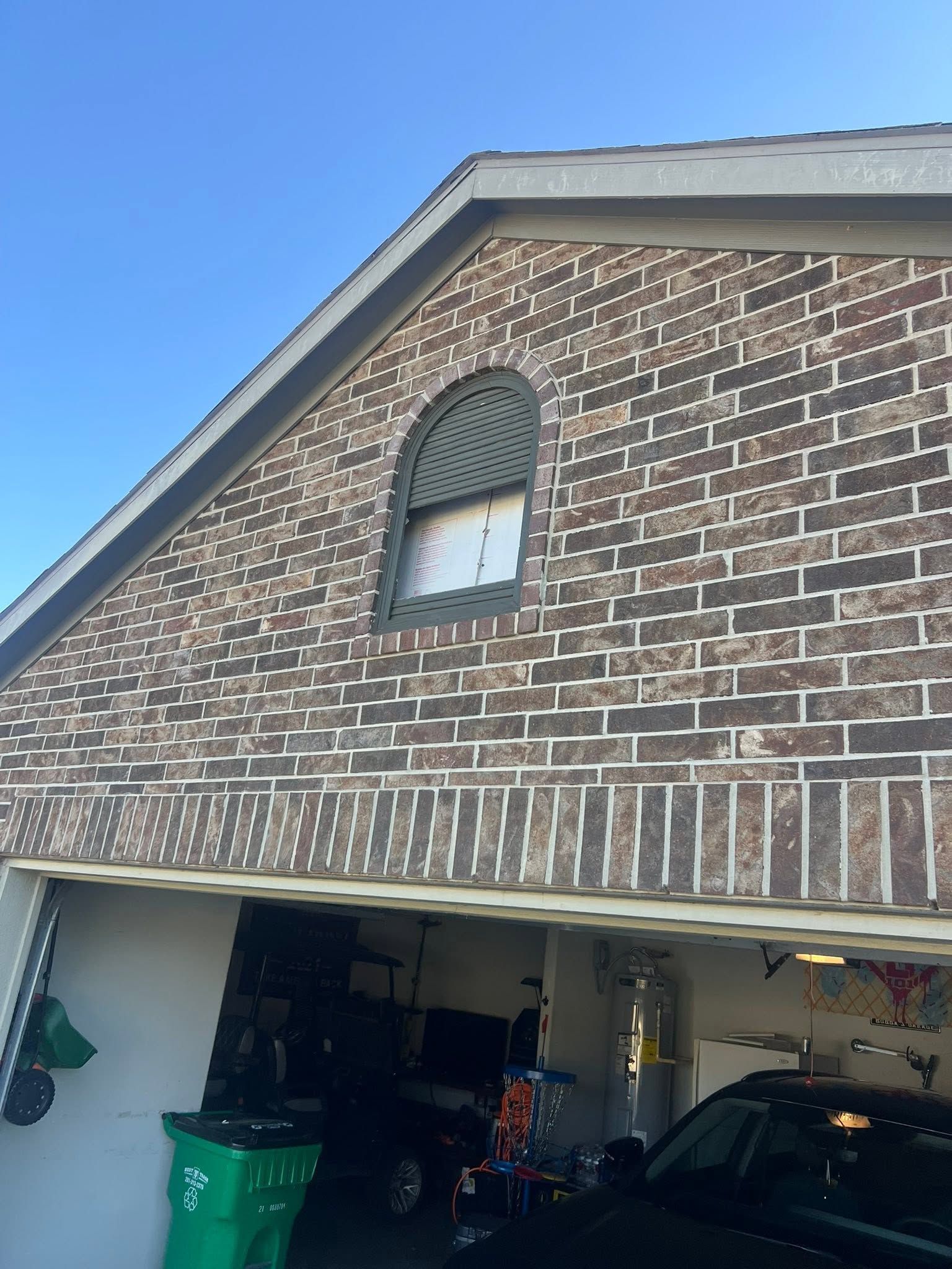 Brick suburban house exterior with arched attic window and open garage below.