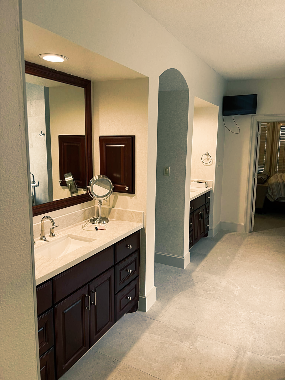 Bathroom vanity with dark wood cabinets, large mirror, and adjacent walk-in closet in a beige room
