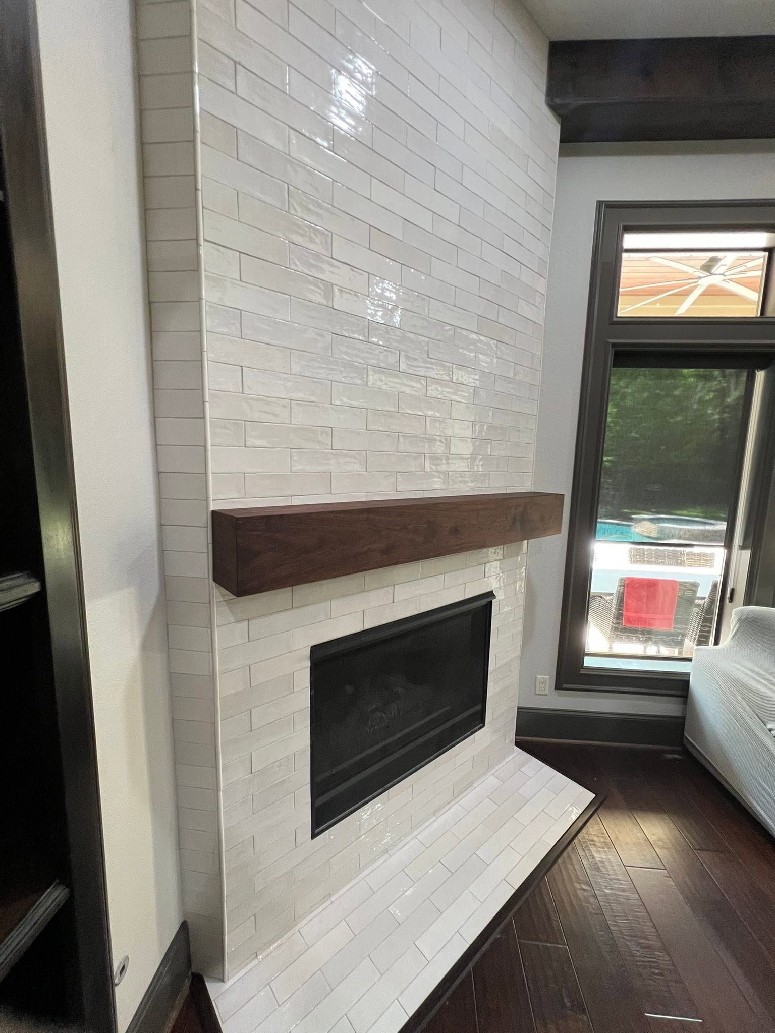White brick fireplace with dark wood mantel in a bright room beside a tall window