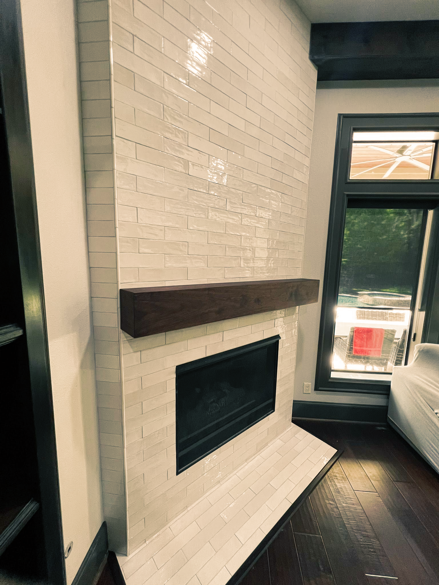 White brick fireplace with dark mantel in a room beside a large window.