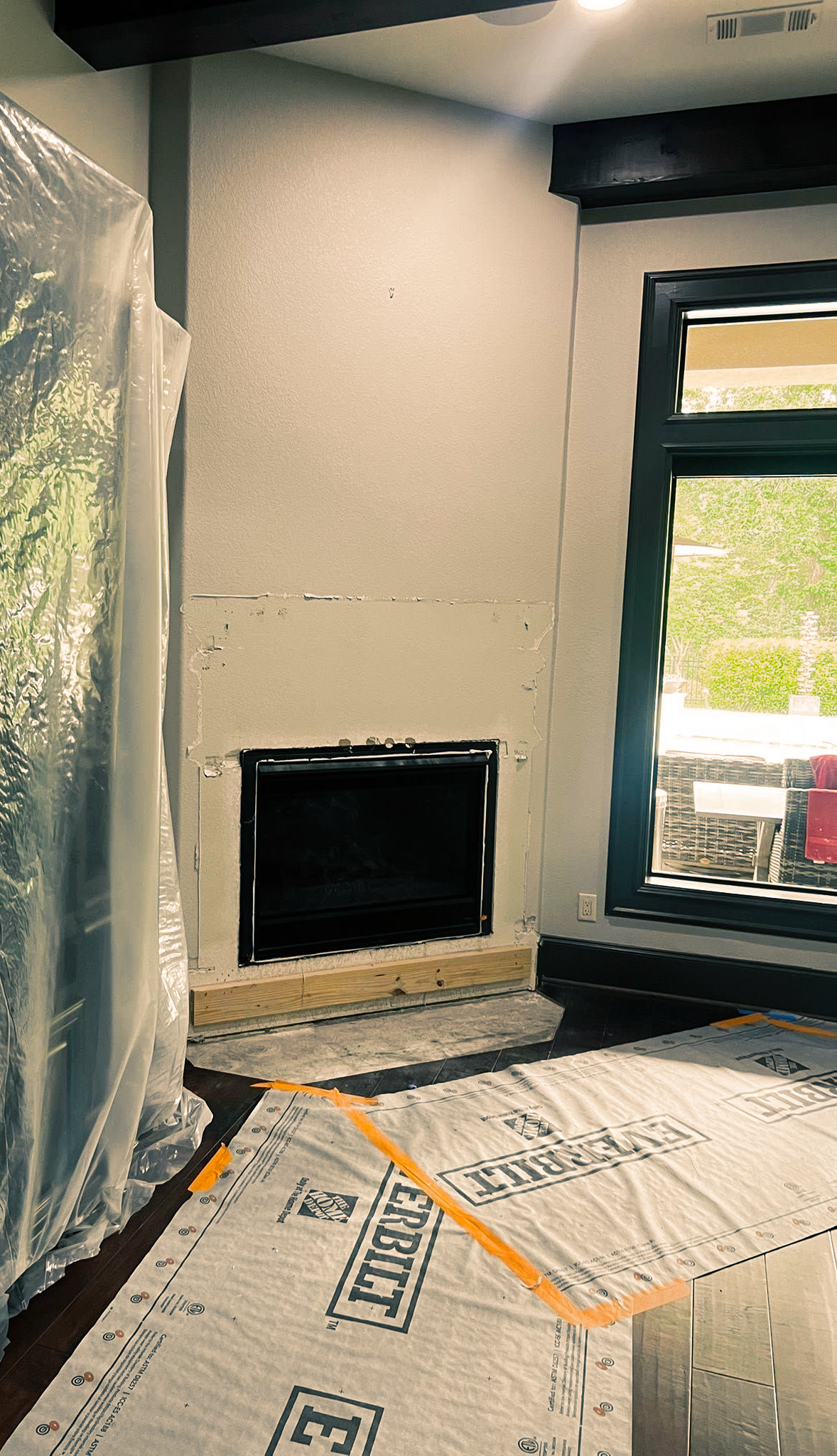 Renovation room with a black fireplace opening, window, and covered floor and walls