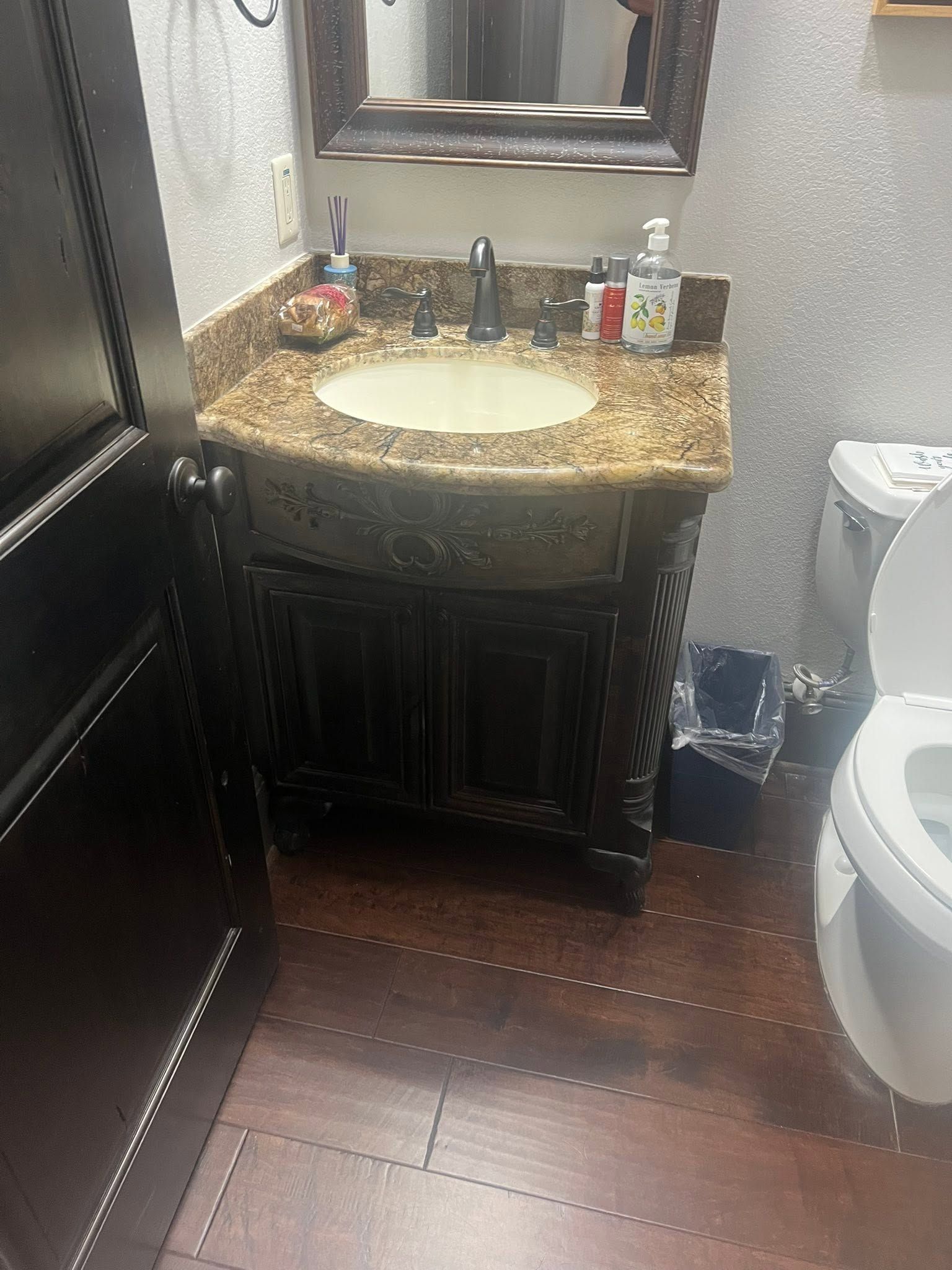Small bathroom with granite vanity, mirror, sink, toiletries, and part of a toilet visible.