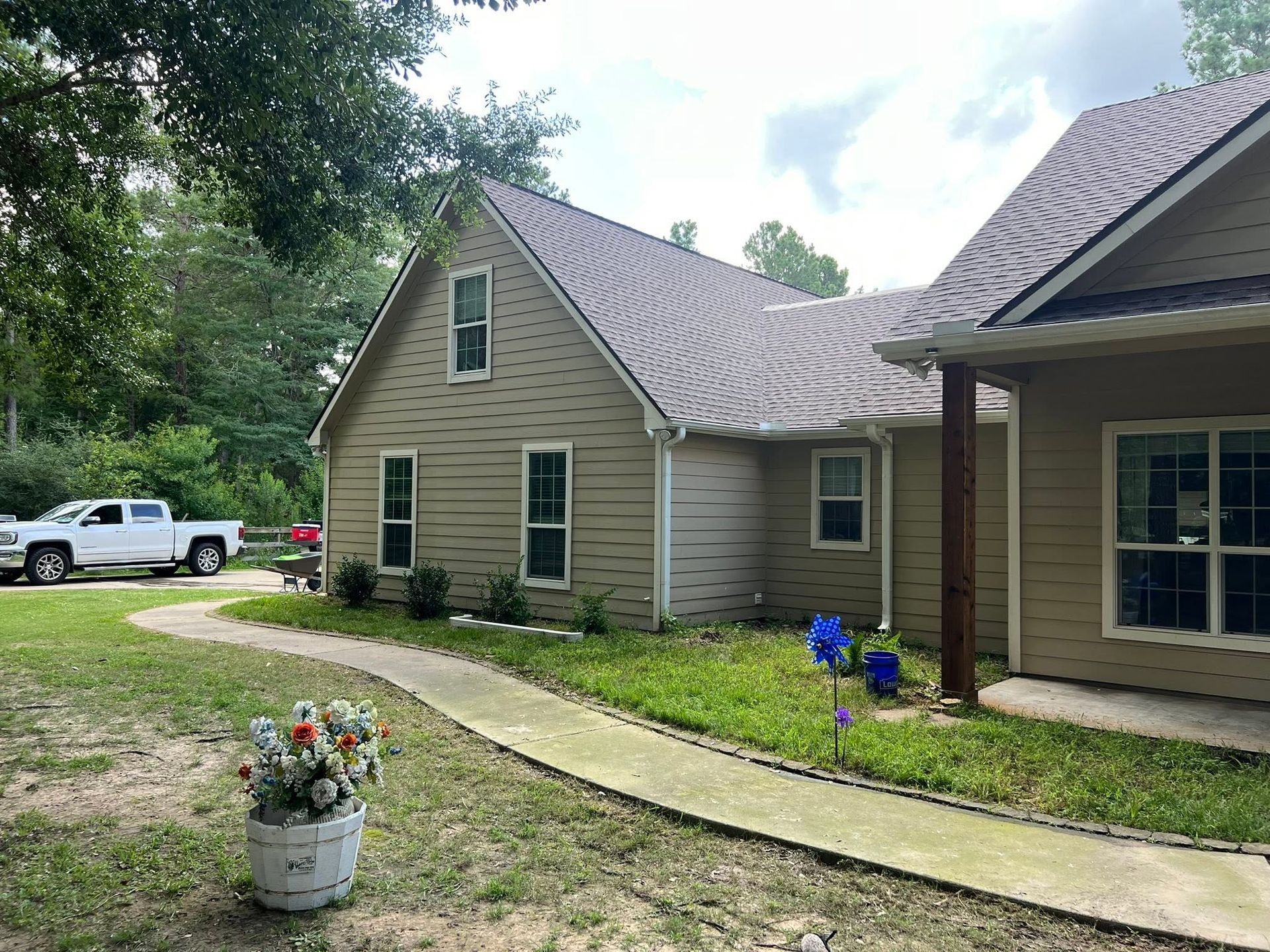 Suburban house exterior with a curved walkway, potted flowers, and a white pickup truck in the driveway