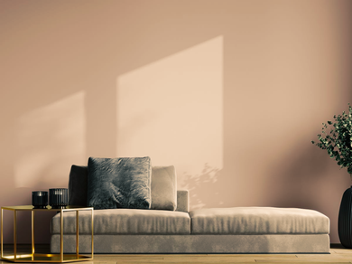 Minimalist living room with a beige sofa, gold side tables, and warm sunlight on a pink wall.