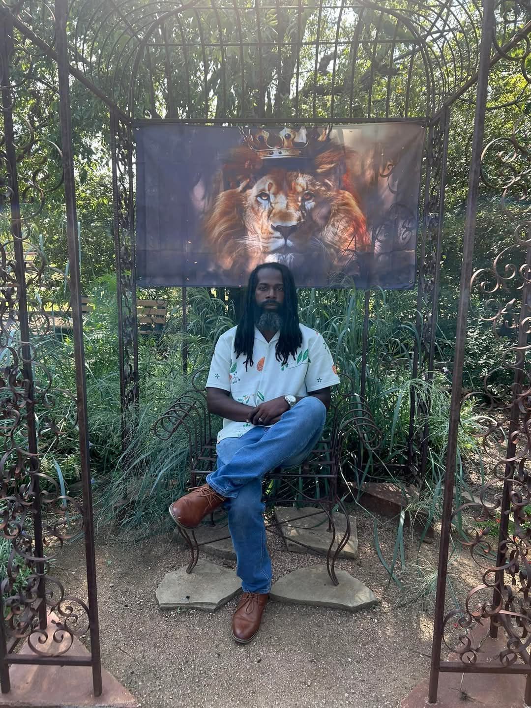 A man with locks is sitting in front of a lion with a crown on its head.