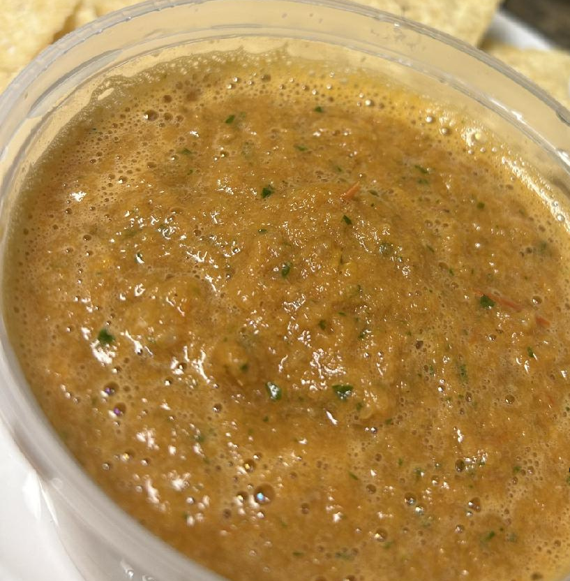 Brown salsa in a clear plastic container, speckled with green, slightly bubbly.