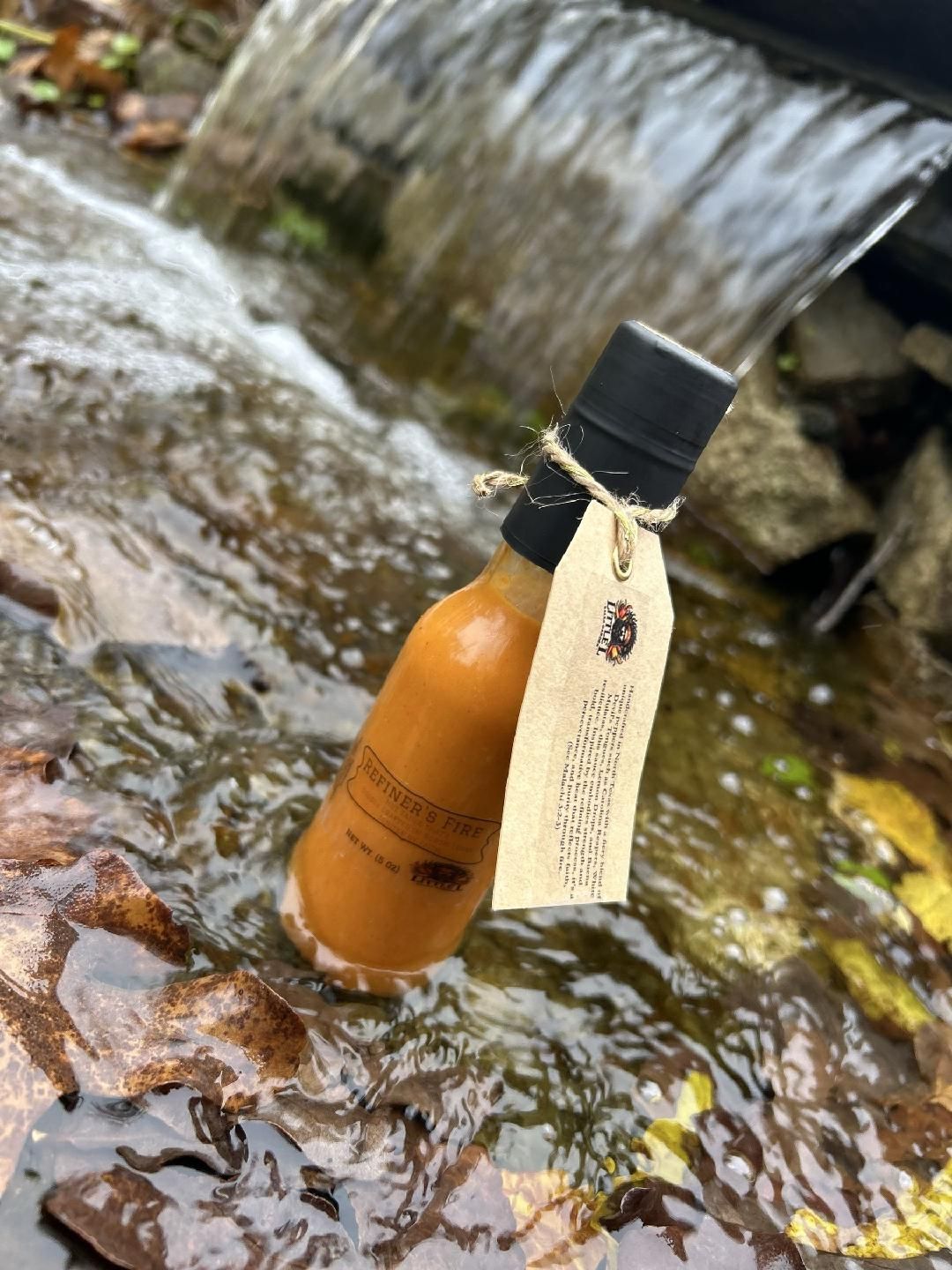 A bottle of hot sauce is sitting on a table next to a plate of food.