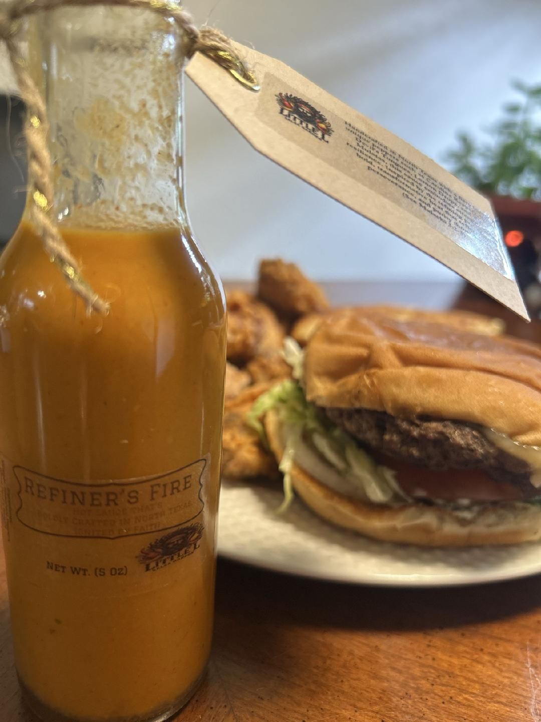 A bottle of hot sauce is sitting on a table next to a plate of food.