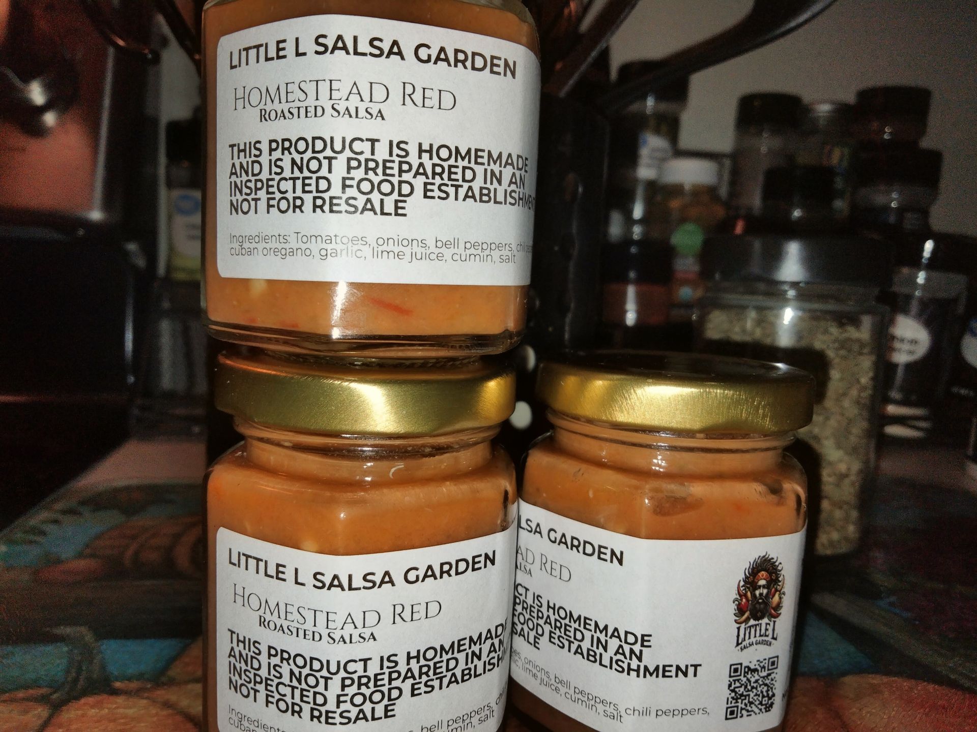 Stacked Little Salsa Garden jars with labels and gold lids on a shelf